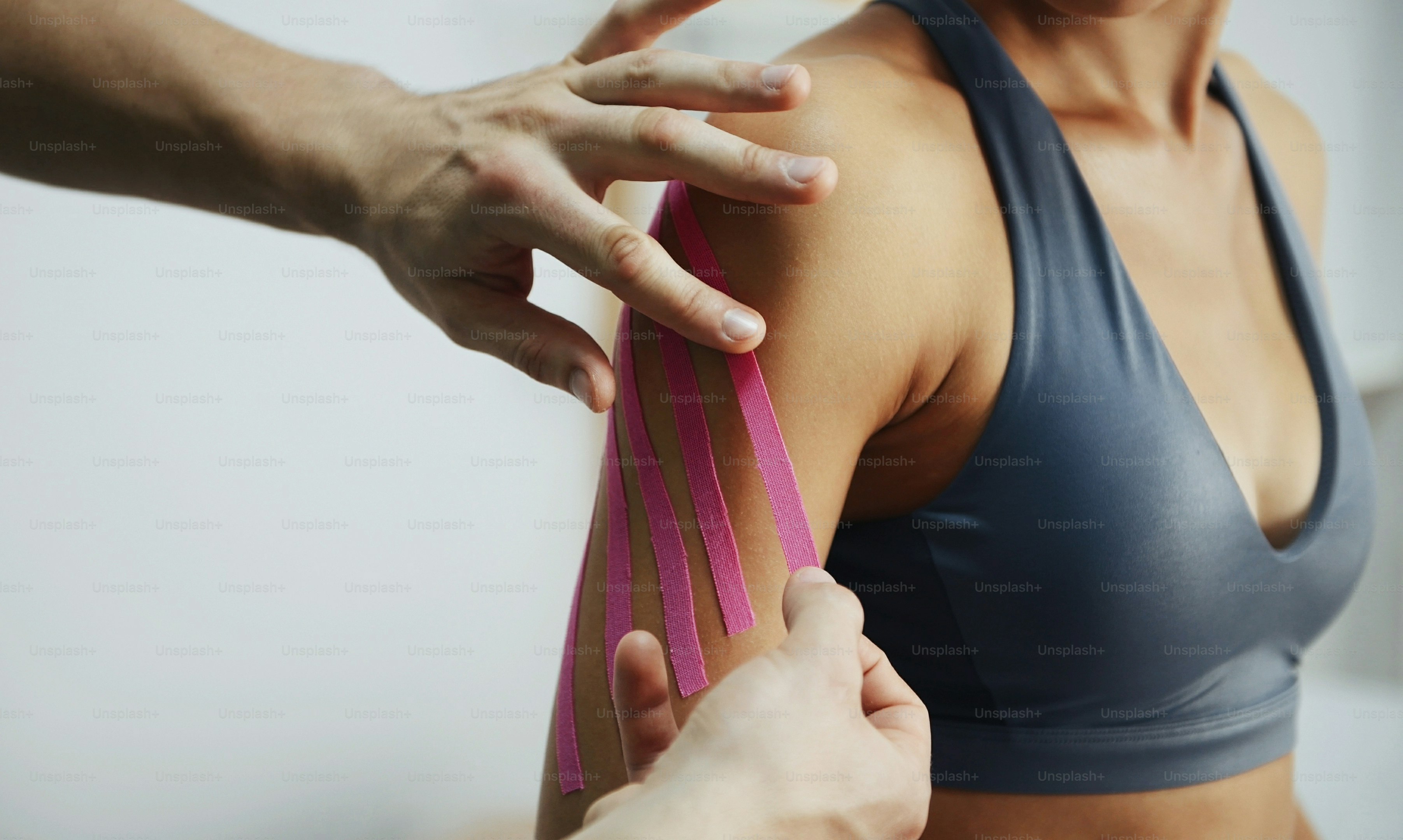 Doctor helps woman by shoulder treatment with kinesio tape.